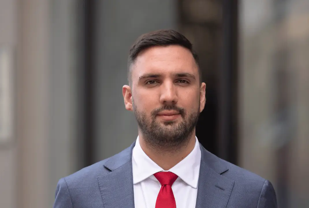 Stefan Simic u sivom odelu i crvenoj kravati stoji ispred zgrade.